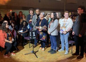 Mary stands at the microphone at the NDP Convention surrounded by her supporters as she delivers her election speech.